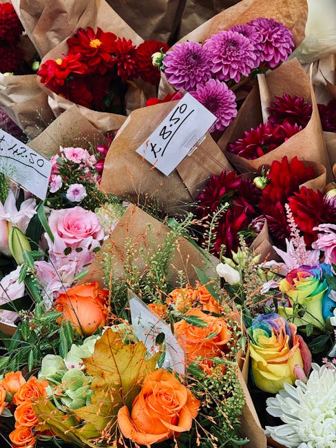 A colorful assortment of fresh flowers arranged in bouquets, including red dahlias, pink chrysanthemums, purple chrysanthemums, peach roses, rainbow roses, and white dahlias. The flowers are wrapped i