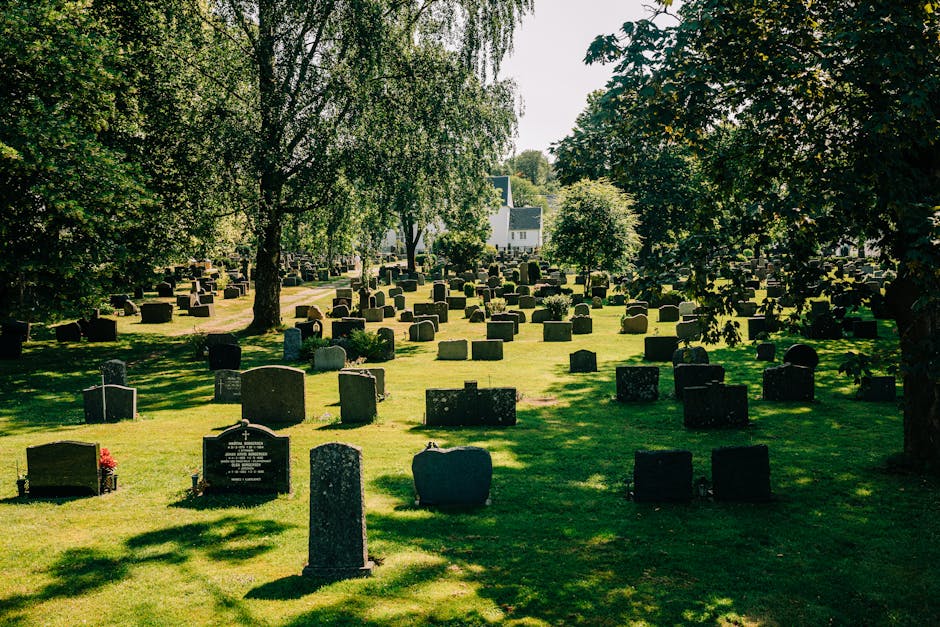 A peaceful cemetery scene in Hornchurch with neatly arranged rows of dark-colored tombstones of various shapes and sizes on a green, well-maintained lawn. Tall leafy trees cast dappled shadows across 